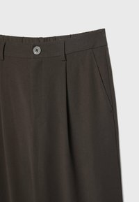 Ciemnobrązowe spodnie o dopasowanym kroju z gładką fakturą, plisowanym przodem i zapięciem na guzik. Posiadają boczne kieszenie oraz klasyczny krój.