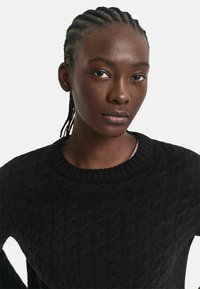 Schwarzer Strickpullover mit Rundhalsausschnitt, der ein strukturiertes Muster und gerippte Bündchen aufweist. Glattes Material mit dezentem Glanz.
