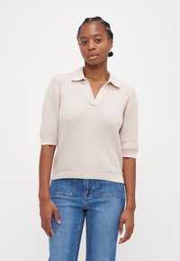 Beige strikket polo genser med kort erme, V-hals og ribbestrikket tekstur, kombinert med blå denimjeans.