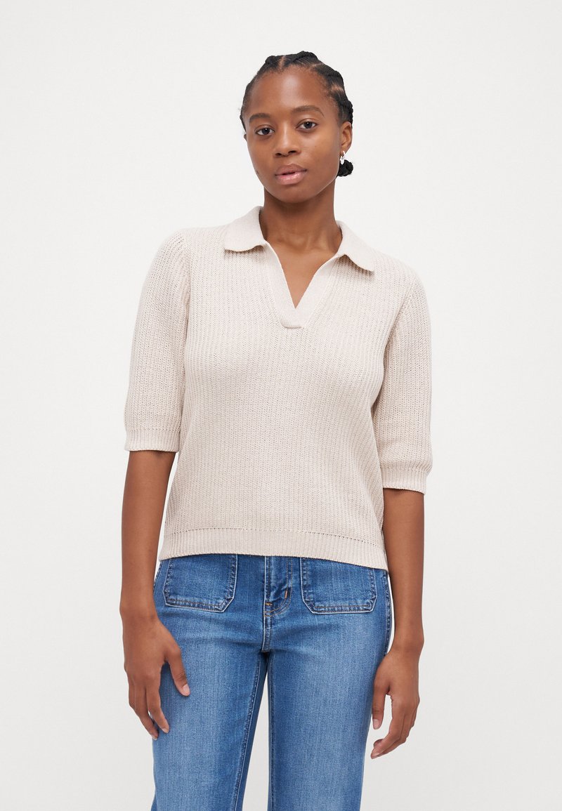 Beige strikket polo genser med kort erme, V-hals og ribbestrikket tekstur, kombinert med blå denimjeans.