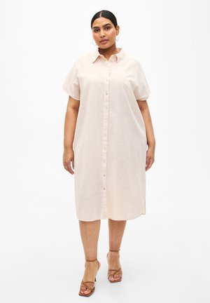 Vestido beige claro de botones con mangas cortas, ajuste holgado, aberturas laterales y textura suave. Combinado con tacones marrones de tiras.