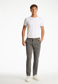 Grijze op maat gemaakte broek met een knoopsluiting en voorzakken, gecombineerd met een aansluitend wit t-shirt en witte sneakers. Glad stofoppervlak.