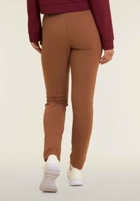 Leggings marroni elasticizzati con design aderente, caratterizzati da una superficie liscia e polsini aderenti, abbinati a scarpe sportive bianche.