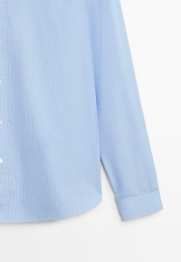 Světle modrá košile s dlouhým rukávem a vertikálním pruhovaným vzorem, zaobleným spodním okrajem, zapínáním na knoflíky vpředu a detaily na manžetách. Hladká textura látky.