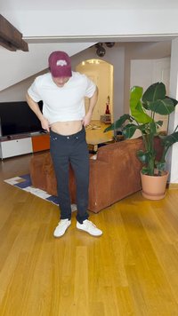 Svarta byxor med en smal passform och synliga sömmar, tillsammans med en vit t-shirt och vita sneakers. Inomhusmiljö med en växt och möbler.