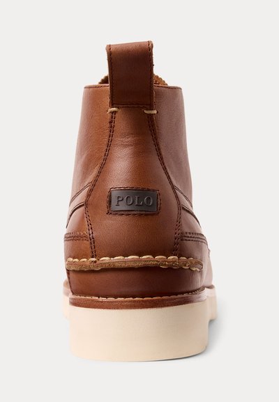 Bruine leren enkellaars met witte zool en treklus, gestikte details en een merklabel "POLO" aan de achterkant.