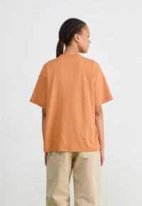 T-shirt en coton texturé, ample, à manches courtes, de couleur orange douce, avec un col rond et un ourlet simple.