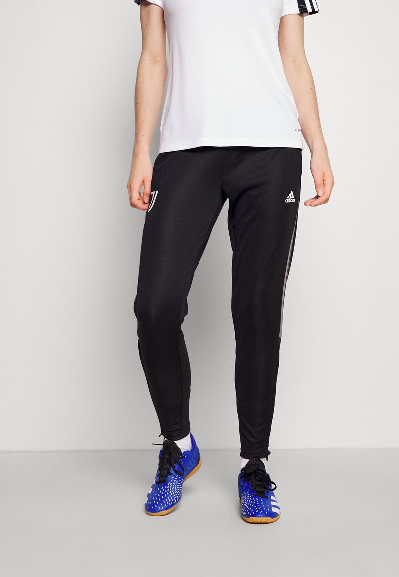 Černé sportovní kalhoty s bílými pruhy po stranách, s logem Juventusu na levém stehně, doplněné modrými sportovními botami.