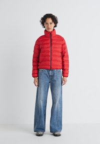 Rode pufferjas met een getailleerd ontwerp, horizontaal gestikt textuur en hoge kraag; gecombineerd met losse blauwe jeans en zwart-witte gestreepte schoenen.