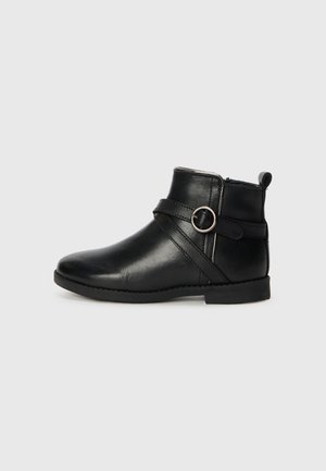 Botte de cheville en cuir noir avec un bout arrondi, une fermeture éclair sur le côté et une sangle décorative avec un accent métallique circulaire. Semelle plate et détails de couture.