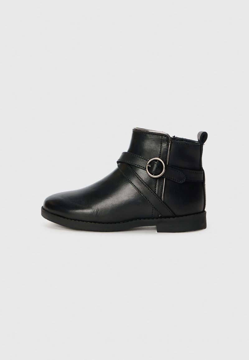 Botte de cheville en cuir noir avec un bout arrondi, une fermeture éclair sur le côté et une sangle décorative avec un accent métallique circulaire. Semelle plate et détails de couture.