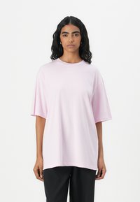Růžové oversized tričko vyrobené z jemné bavlny. Má kulatý výstřih, krátké rukávy a volný střih. Hladká textura bez viditelných vzorů.