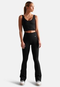 Zwarte geribbelde crop top gecombineerd met hooggeknoopte zwarte leggings, beide met een strakke pasvorm en naadloos ontwerp. Witte platform sneakers maken de look compleet.