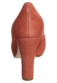 Röda mockaskor med hög klack, spetsig tå och en måttlig klackhöjd. Ytan är slät med en matt finish.