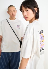 White oversized t-shirts with graphic prints on the front and back. One features a colorful design; the other has text. Both have short sleeves.
