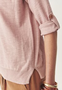 Maglione a maglia leggera di colore rosa chiaro, con maniche arrotolate e dettagli in bottoni di legno. Presenta un orlo a costine e spacchi laterali per un tocco di texture in più.