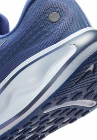 Scarpa sportiva con tomaia strutturata di un blu scuro, suola in gomma, imbottitura prominente, un accento circolare vicino al tallone e un design aerodinamico.