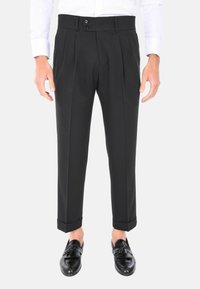 Pantaloni neri plissettati con vestibilità su misura, dotati di due bottoni in vita e orli con risvolto, abbinati a mocassini neri.