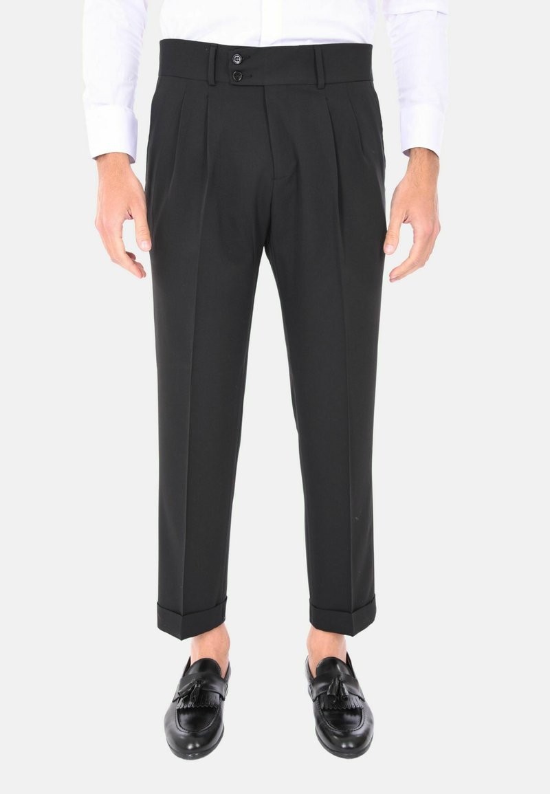Pantaloni neri plissettati con vestibilità su misura, dotati di due bottoni in vita e orli con risvolto, abbinati a mocassini neri.