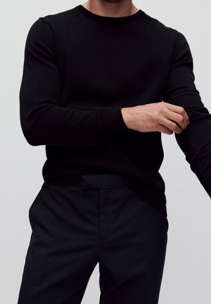 Suéter de punto negro con cuello redondo y mangas largas, combinado con pantalones oscuros, que destaca un diseño ajustado y una textura suave.