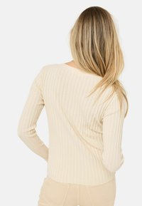 Lichtbeige ribbed lange mouwen top met een nauwsluitend ontwerp en een brede halslijn, voorzien van subtiele verticale lijnen en een textuurafwerking.