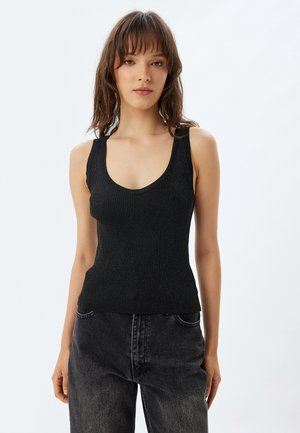 Camisole nera a coste realizzata in materiale elasticizzato, con scollo a barca e spalline larghe. Abbinata a jeans scuri.
