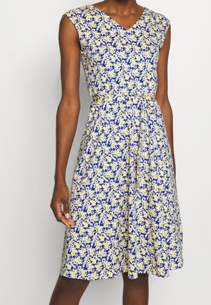 Robe sans manches longueur genou avec décolleté en V, taille cintrée, en tissu bleu à motif de petites fleurs jaunes et blanches.