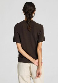 Maglione corto in maglia marrone con texture a costine, caratterizzato da un collo rotondo e un orlo aderente, indossato con pantaloni di colore chiaro.