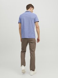 Polo shirt in lichtblauw met een gestructureerde afwerking en zwarte kraagaccenten, gecombineerd met bruine broeken en witte sneakers, gezien vanuit de achterkant.