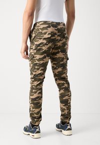 Camouflage cargobroek in groen en beige, met een elastische tailleband en elastische boorden, voorzien van zij- en achterzakken.