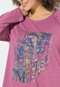 Maglietta a maniche lunghe viola con un design grafico multicolore e le parole "DANCE MAGIC" in caratteri in grassetto. Tessuto morbido al tatto.