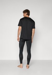 Svart tränings-t-shirt med korta ärmar och reflekterande detaljer, kombinerad med svarta åtsittande tights i ett mjukt, elastiskt material.