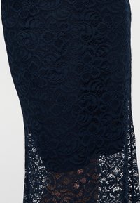 Donkerblauwe rok met een ingewikkeld bloemmotief van kant en een halfdoorzichtig zoomdetail tegen een lichte achtergrond.