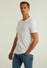 Tricou alb din bumbac, cu mâneci scurte, guler rotund și un logo subtil pe piept. Pur tată cu blugi negri. Textură netedă.