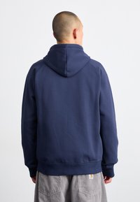 Mørkeblå hettegenser med stor, justerbar hette, strikkede mansjetter og kant. Myk tekstur, minimalistisk design og ingen synlige logoer eller mønstre.