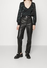 Svart blommönstrad blus med djup V-urringning och spetsdetaljer, ihopparad med högmidjade, släta svarta läderbyxor och svarta skor.