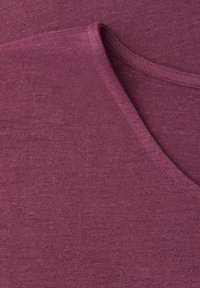 Primo piano di tessuto lavorato a maglia viola piegato che mostra la trama e le cuciture intorno a un bordo curvo.