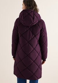 Cappotto imbottito trapuntato viola con un grande cappuccio, caratterizzato da un motivo a diamante e polsini a costine, che arriva fino a metà coscia.