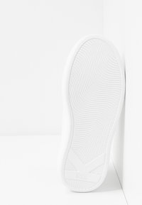 Semelle de chaussure en caoutchouc blanc avec un motif ondulé texturé et une marque. Forme arrondie avec des bords lisses ; conçue pour l'adhérence et la stabilité.