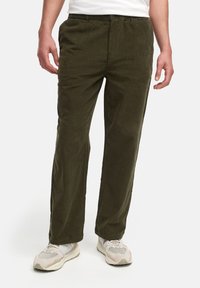 Pantalones de pana verde oliva con un corte relajado. Cuentan con un cierre de botón y bolsillos laterales, tela texturizada y piernas rectas.