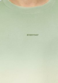 Lichtgroene sweatshirt met geribbelde ronde hals, voorzien van een subtiele gradient en het woord 'EVERYDAY' in donkergroen gedrukt.