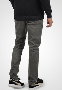 Szare legginsy o fakturowanej tkaninie, w wąskim kroju, z bocznymi kieszeniami, w połączeniu z czarnymi sneakersami z złotymi akcentami.