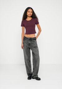 T-shirt cropped bordeaux con maniche corte, abbinata a jeans grigi a taglio largo e vita alta, e scarpe nere. Design semplice con dettagli minimi.