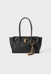 Black leather handbag with double handles, gold lock and chain detail, and black-and-white tassel accessory against white background.