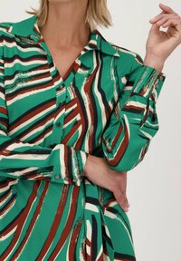 Groene multikleurige jurk met gedurfde strepen in crème, bruin en marineblauw. Lange mouwen met knoopmanchetten en een puntige kraag.