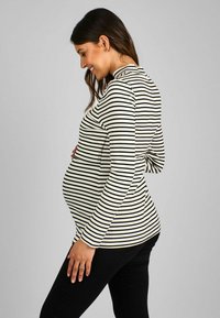 Schwarz-weiß gestreifte, figurbetonte Langarmbluse aus Rippstoff, getragen über einem runden Bauch, kombiniert mit schwarzen Hosen.