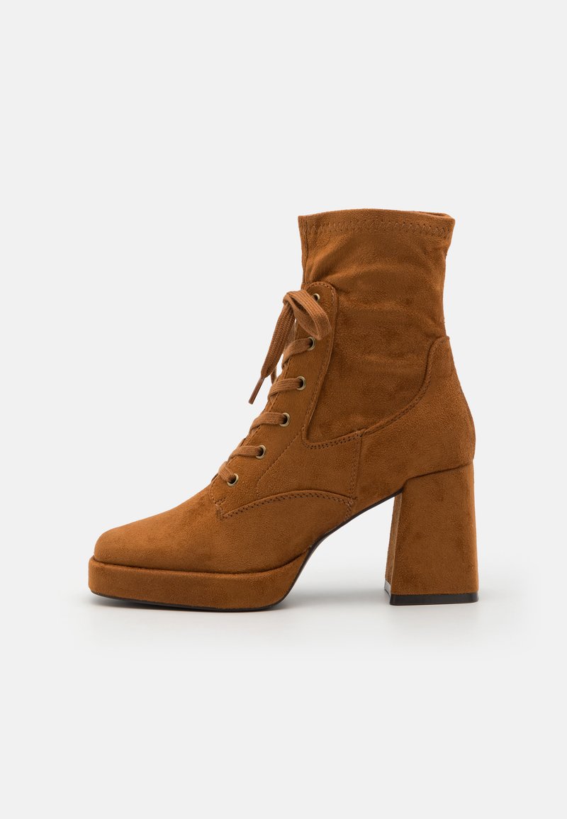 Bottine en daim marron avec un bout arrondi, un col rembourré et un laçage à l'avant. Elle présente un talon carré épais et une finition texturée.