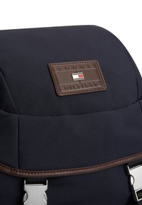 Σκούρο μπλε υφασμάτινο σακίδιο με καφέ δερμάτινη ετικέτα που φέρει το λογότυπο. Ασημένιες μεταλλικές λεπτομέρειες στα λουριά. Λεπτή υφή με δομημένο σχήμα.