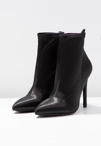 Bottes noires chevilles avec des bouts pointus, des talons aiguilles hauts et une finition lisse et élégante. Conçues sans fermetures visibles ni ornements.