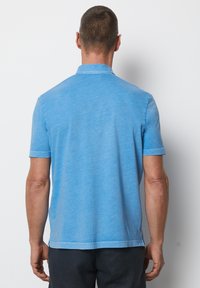 Helles blaues Polohemd mit kurzen Ärmeln und flachem Kragen, aus strukturiertem Stoff gefertigt. Mit geradem Saum und dezenten Steppnähten.